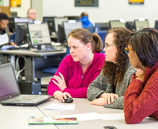 Image of three woman looking and at a computer and having a discussion