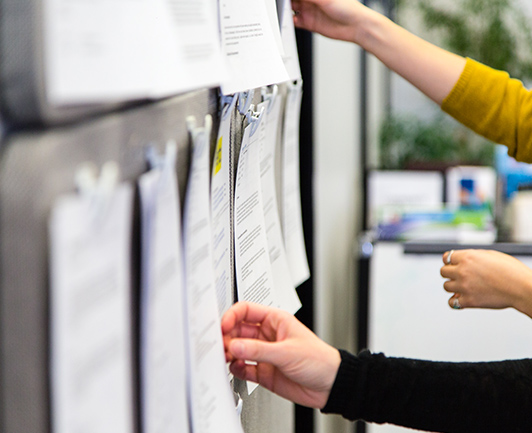 Image of people's hand grabbing papers hanging on the wall for Jobs page