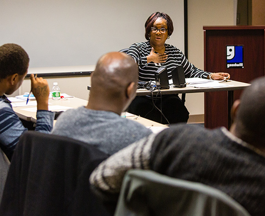 Image of woman sitting at a table and speaking to an audience