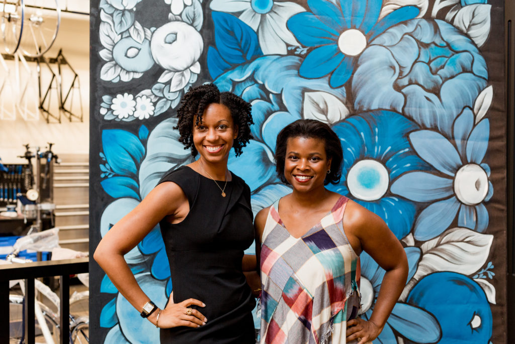 Two woman gather in front of a mural painted by local artist, 0uizi, at the SP reception at Shinola.